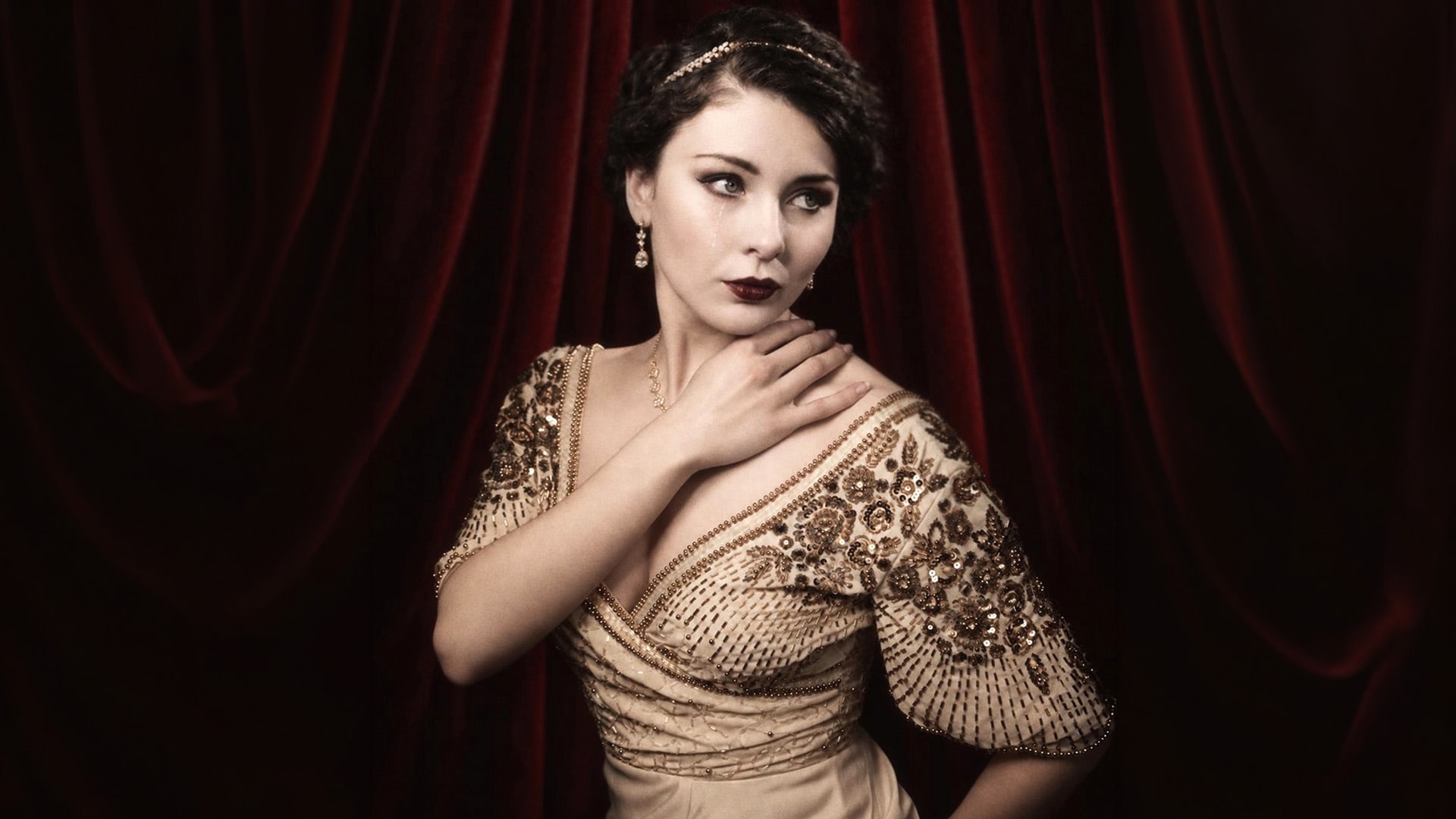 Megan Tremethick in a beaded evening gown against red theatre curtains